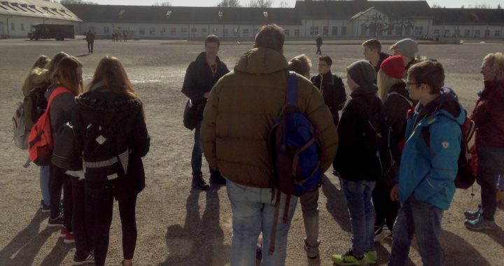 Die Montessori-Klasse 9/10 auf dem Appellplatz bei Ihrer Führung durch die KZ-Gedenkstätte Dachau. Im Hintergrund sieht man das Wirtschaftsgebäude und die mahnenden Kunstwerke der Überlebenden.